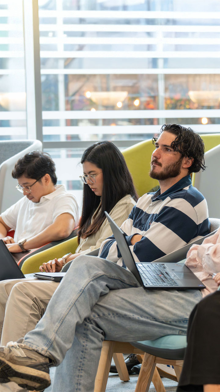 A group of young audit students listening to a presentation in a bright modern office.