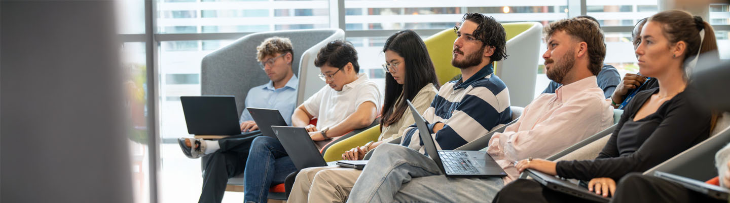 A group of young audit students listening to a presentation in a bright modern office.
